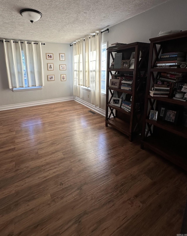 spare room with visible vents, a textured ceiling, baseboards, and wood finished floors