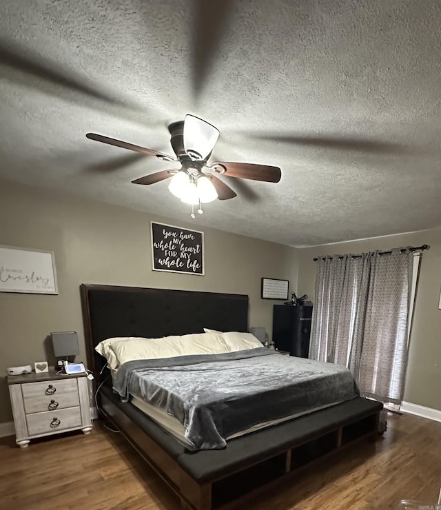 bedroom with a ceiling fan, a textured ceiling, baseboards, and wood finished floors