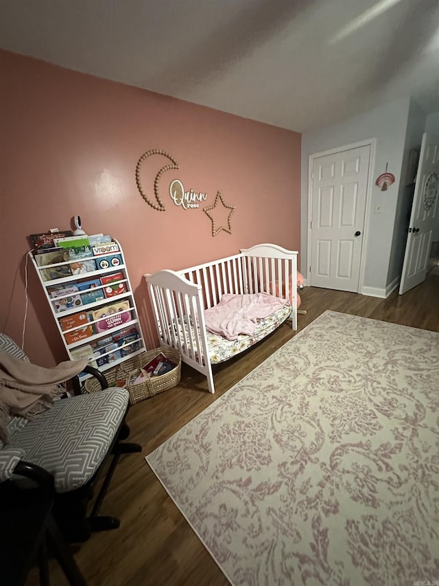 bedroom featuring a nursery area, baseboards, and dark wood finished floors