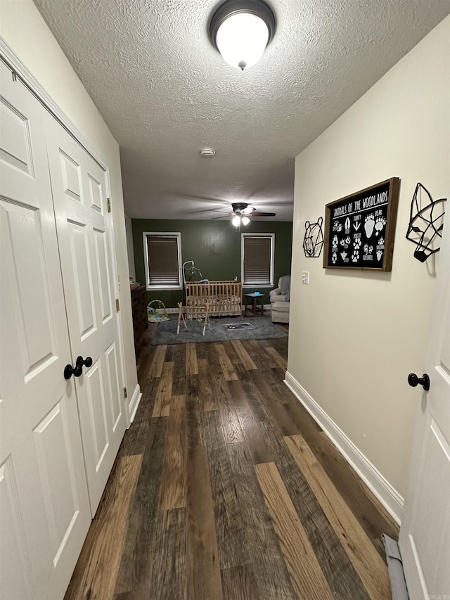 hall featuring a textured ceiling, baseboards, and dark wood-type flooring