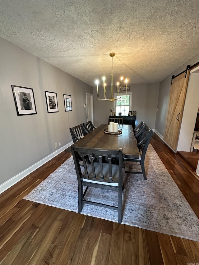 dining room with a chandelier, a textured ceiling, a barn door, dark wood-type flooring, and baseboards