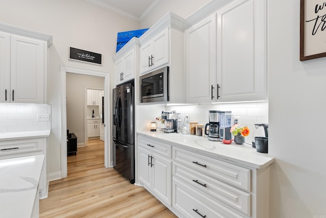 kitchen featuring white cabinets, light wood-type flooring, freestanding refrigerator, built in microwave, and crown molding