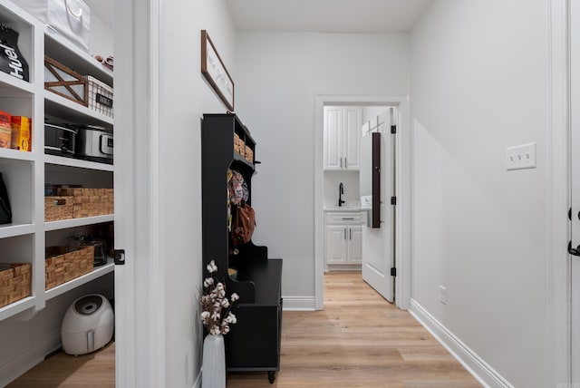 hall with baseboards, a sink, and light wood finished floors