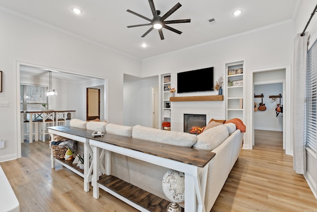 living area featuring a glass covered fireplace, visible vents, crown molding, and light wood finished floors