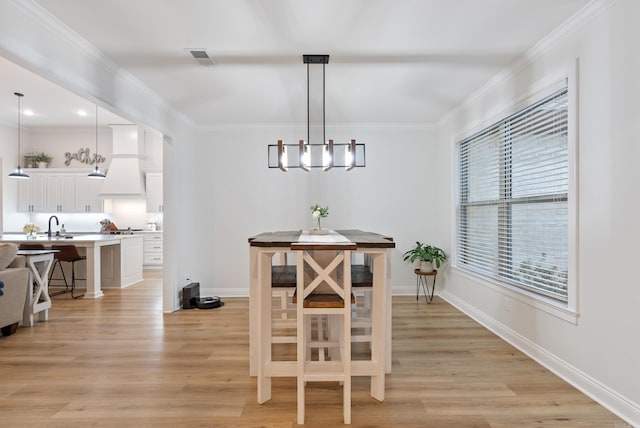 dining space featuring light wood-type flooring, crown molding, and baseboards