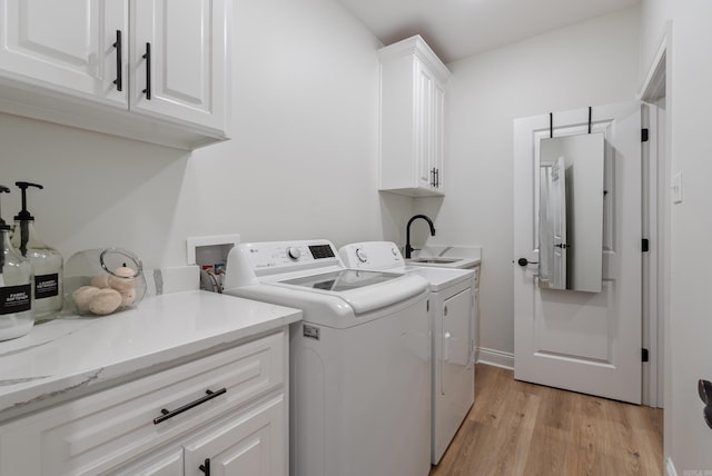 washroom with cabinet space, a sink, light wood-style flooring, and washing machine and clothes dryer