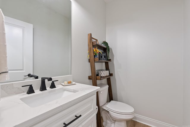 half bathroom featuring toilet, baseboards, wood finished floors, and vanity