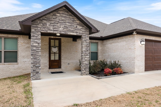 doorway to property featuring brick siding, an attached garage, and roof with shingles