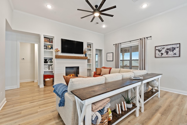 living room featuring ornamental molding, light wood-type flooring, a glass covered fireplace, and a ceiling fan