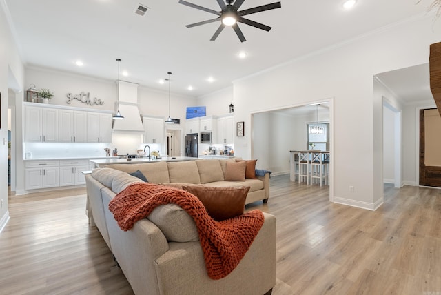 living area featuring baseboards, visible vents, a ceiling fan, ornamental molding, and light wood-type flooring