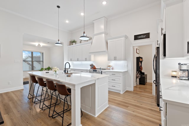 kitchen featuring premium range hood, a breakfast bar, a sink, appliances with stainless steel finishes, and crown molding