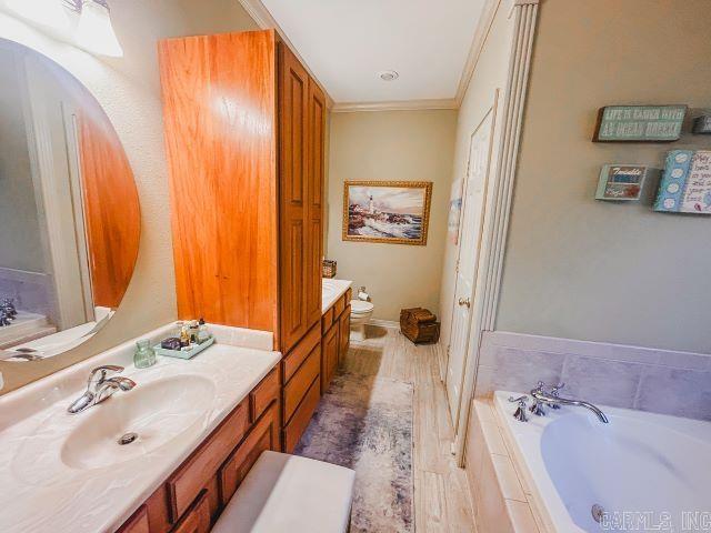 full bathroom with toilet, a garden tub, ornamental molding, and vanity