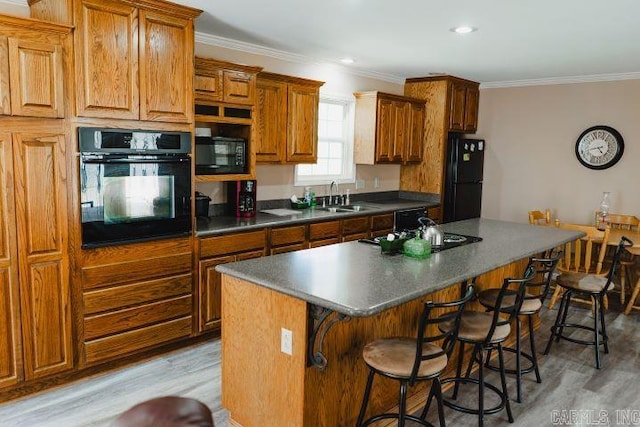 kitchen featuring a breakfast bar, a sink, ornamental molding, a center island, and black appliances