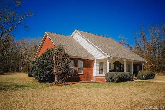 view of front of house featuring a front yard, brick siding, and roof with shingles