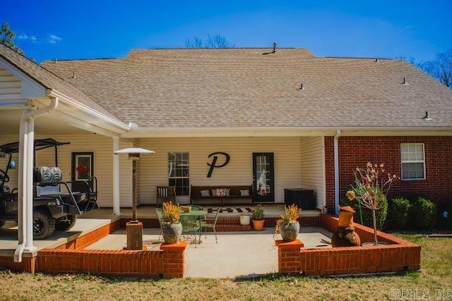 rear view of house featuring a patio area, roof with shingles, brick siding, and an outdoor hangout area