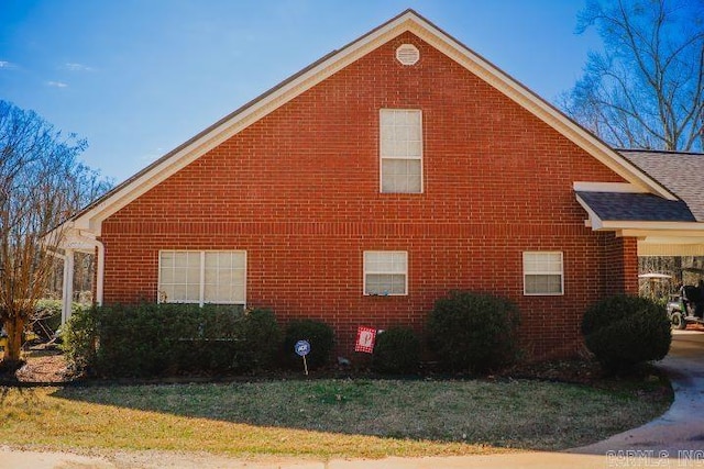 view of home's exterior with a shingled roof, brick siding, and a yard