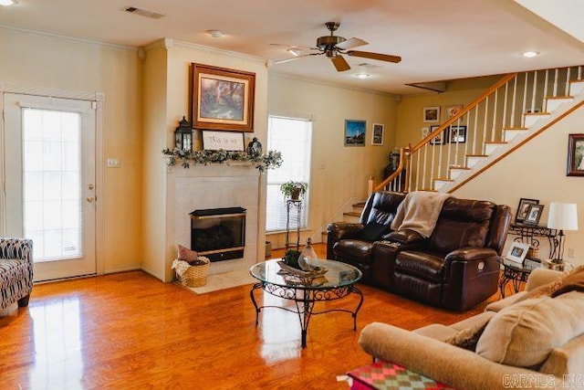 living area with a fireplace with flush hearth, wood finished floors, visible vents, ornamental molding, and stairway