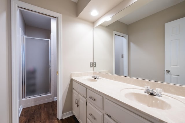 full bathroom with double vanity, a shower stall, a sink, and wood finished floors