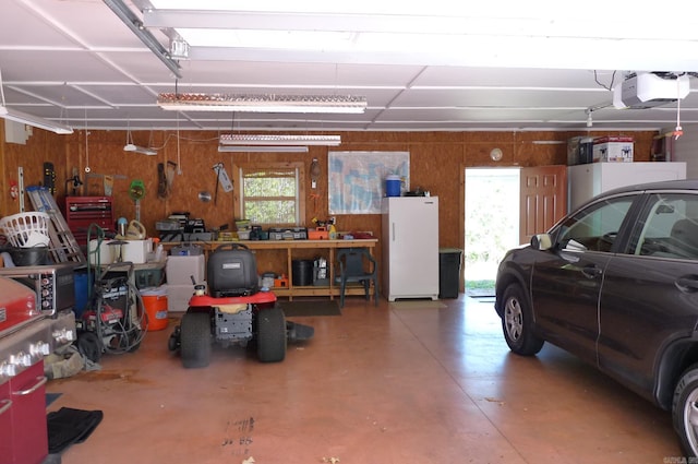 garage with wood walls, freestanding refrigerator, a workshop area, and a garage door opener