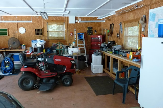 garage featuring freestanding refrigerator, wooden walls, and a workshop area