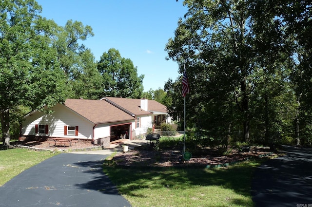 view of front of home featuring aphalt driveway, a front yard, a chimney, and an attached garage