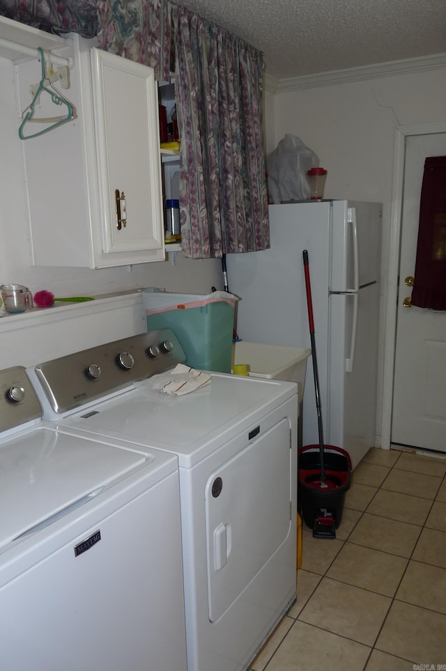 clothes washing area with light tile patterned floors, a textured ceiling, separate washer and dryer, ornamental molding, and cabinet space