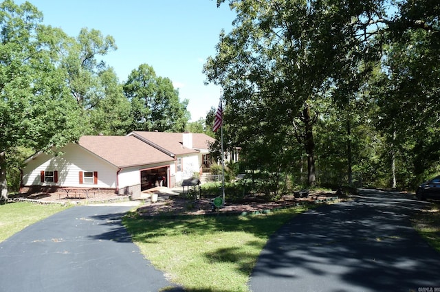 view of front facade with aphalt driveway, a chimney, and a front yard