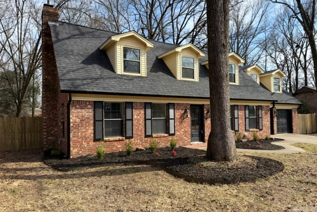 new england style home featuring a shingled roof, concrete driveway, brick siding, and fence