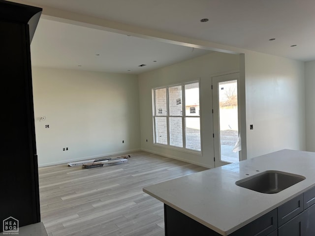 kitchen featuring a sink, baseboards, open floor plan, light countertops, and light wood-type flooring