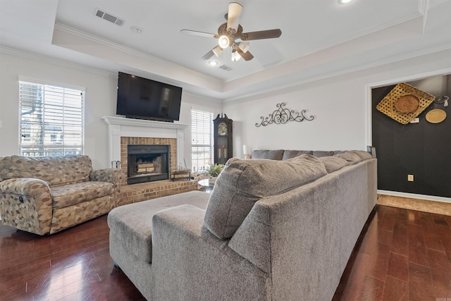 living room with dark wood-style floors, visible vents, a raised ceiling, and ornamental molding