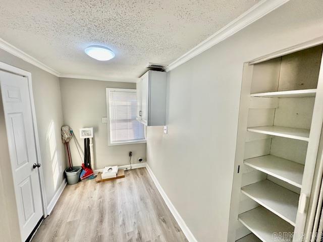 clothes washing area with a textured ceiling, laundry area, baseboards, light wood-style floors, and ornamental molding