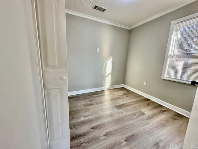 spare room featuring baseboards, visible vents, ornamental molding, wood finished floors, and a textured ceiling