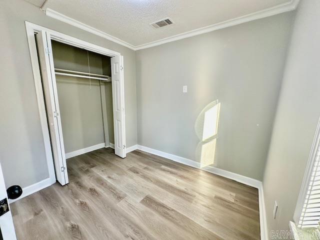 unfurnished bedroom with baseboards, visible vents, wood finished floors, crown molding, and a textured ceiling