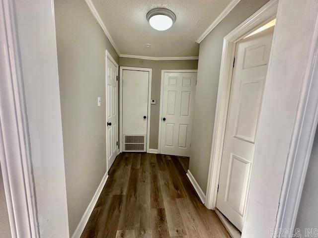 hall featuring a textured ceiling, wood finished floors, visible vents, baseboards, and crown molding