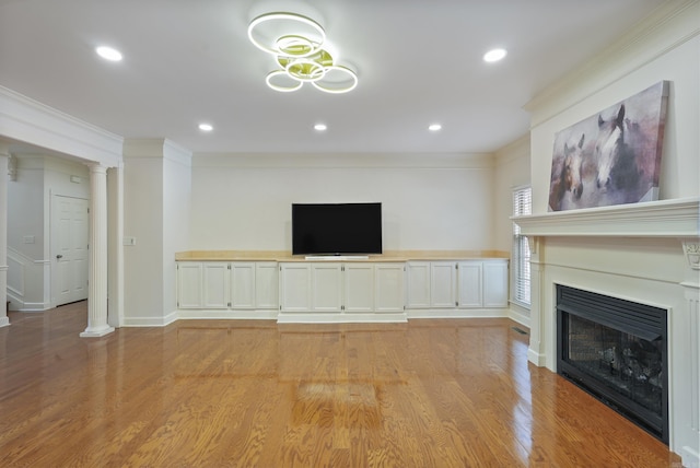 unfurnished living room with ornamental molding, a fireplace, decorative columns, and light wood-style flooring