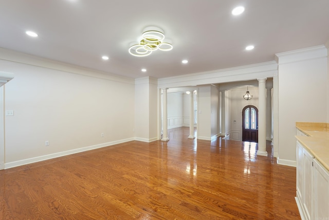 unfurnished living room with ornamental molding, arched walkways, ornate columns, and wood finished floors