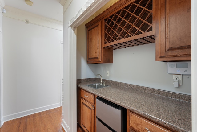 kitchen featuring wood finished floors, a sink, baseboards, freestanding refrigerator, and brown cabinets