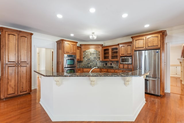 kitchen with brown cabinetry, a breakfast bar area, stainless steel appliances, and wood finished floors