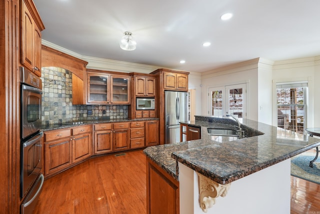 kitchen featuring stainless steel appliances, wood finished floors, a sink, brown cabinetry, and crown molding