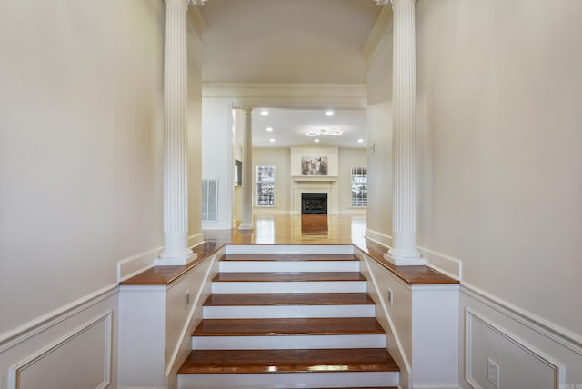 stairs featuring ornate columns, a fireplace, and a decorative wall