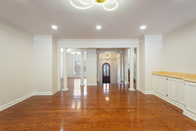 hallway with crown molding, decorative columns, baseboards, and wood finished floors