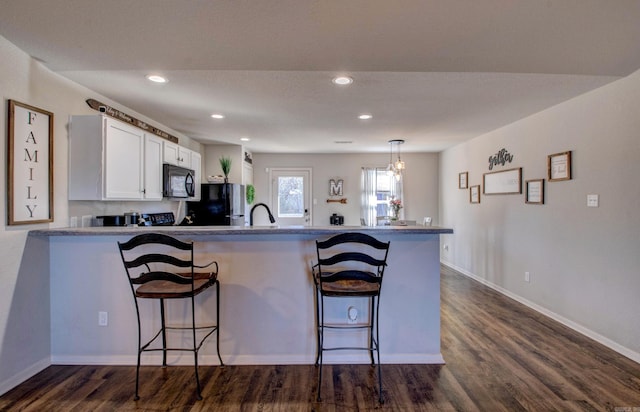 kitchen with dark wood finished floors, a breakfast bar area, white cabinets, a peninsula, and black appliances