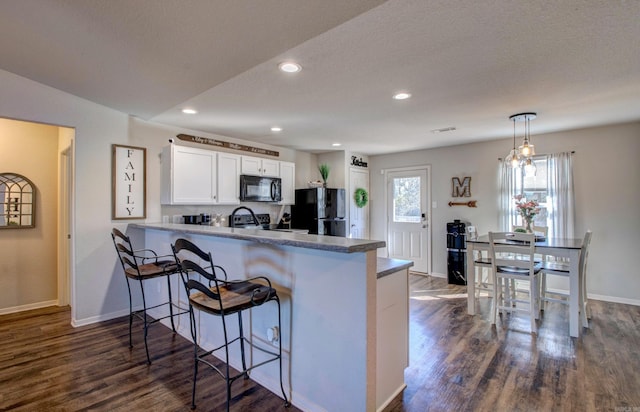 kitchen with a peninsula, black appliances, white cabinetry, and dark wood-style flooring