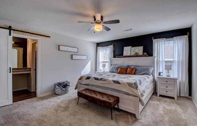 bedroom with light carpet, visible vents, a textured ceiling, and a barn door