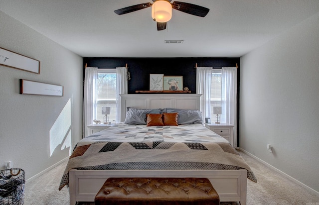 carpeted bedroom with a textured wall, visible vents, ceiling fan, and baseboards