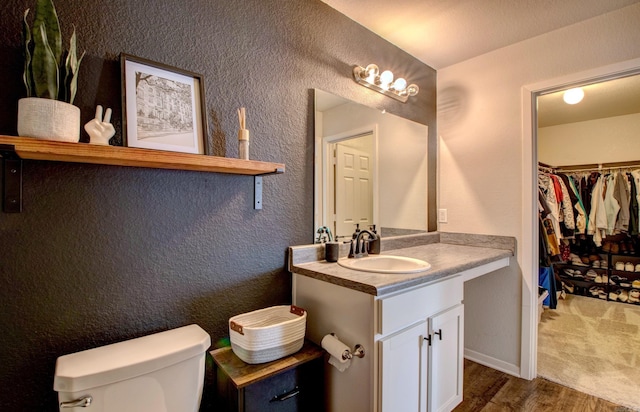 bathroom with a textured wall, toilet, wood finished floors, a walk in closet, and vanity