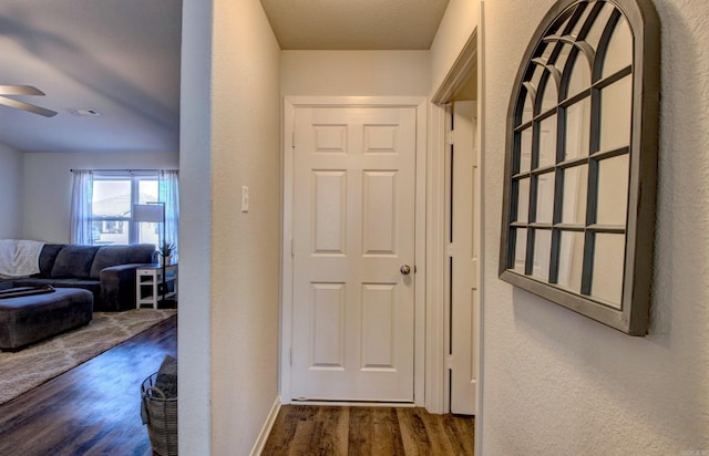 corridor featuring visible vents, a textured wall, baseboards, and wood finished floors