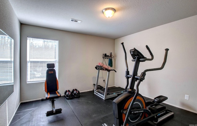 exercise area with a textured ceiling, visible vents, and baseboards