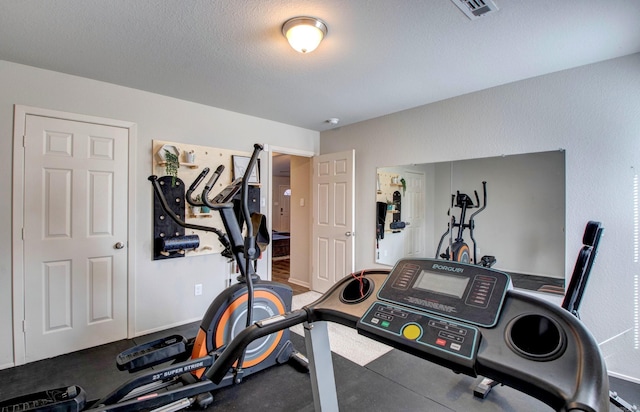 exercise room featuring visible vents, a textured ceiling, and baseboards