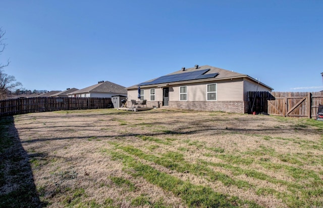 back of property featuring a yard, a fenced backyard, solar panels, and brick siding